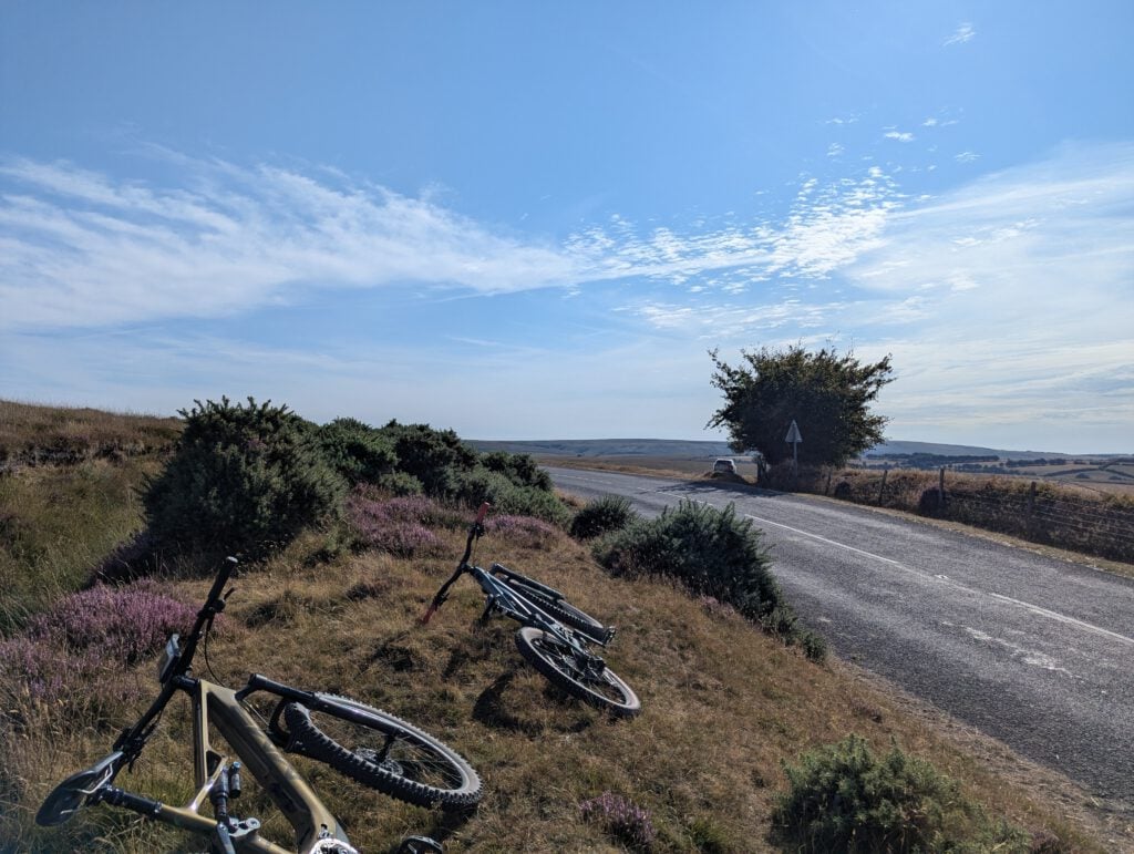 Two mountain bikes laid down in heather beside a quiet moorland road